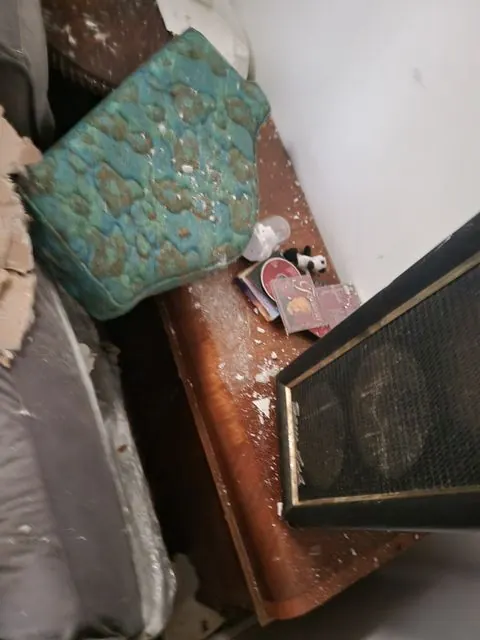 A jumble of water-damaged belongings in one frame: a ceramic planter, a framed picture and a wooden cabinet