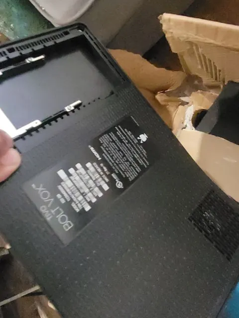 An adjuster holding a flat-screen television steady to photograph the model plate on its back